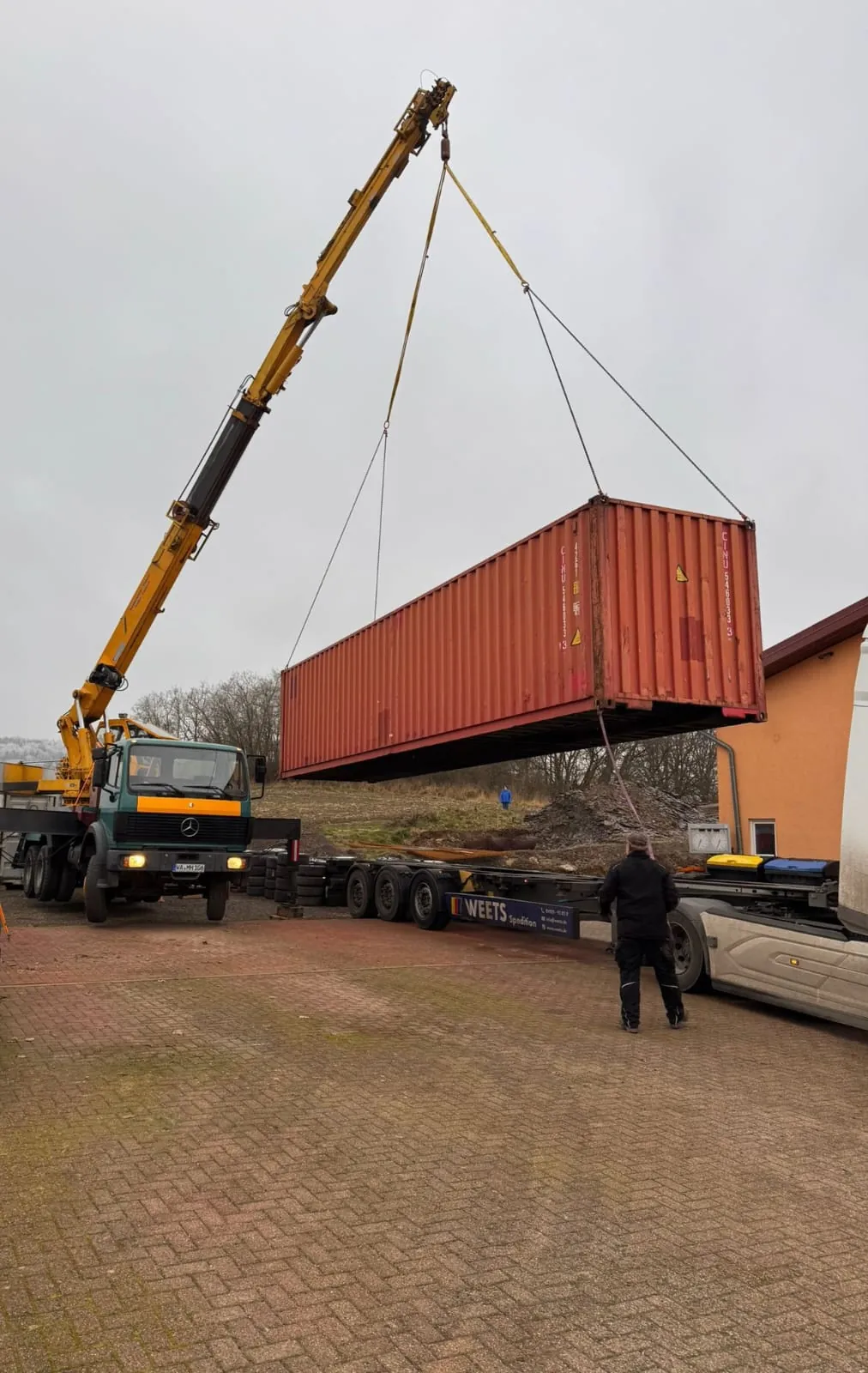 Milanik Autokran hebt einen Übersee-Container von einem Tieflader